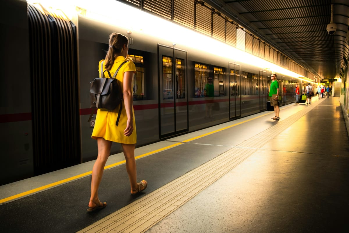 A woman in a yellow dress with a backpack walking along a metro platform